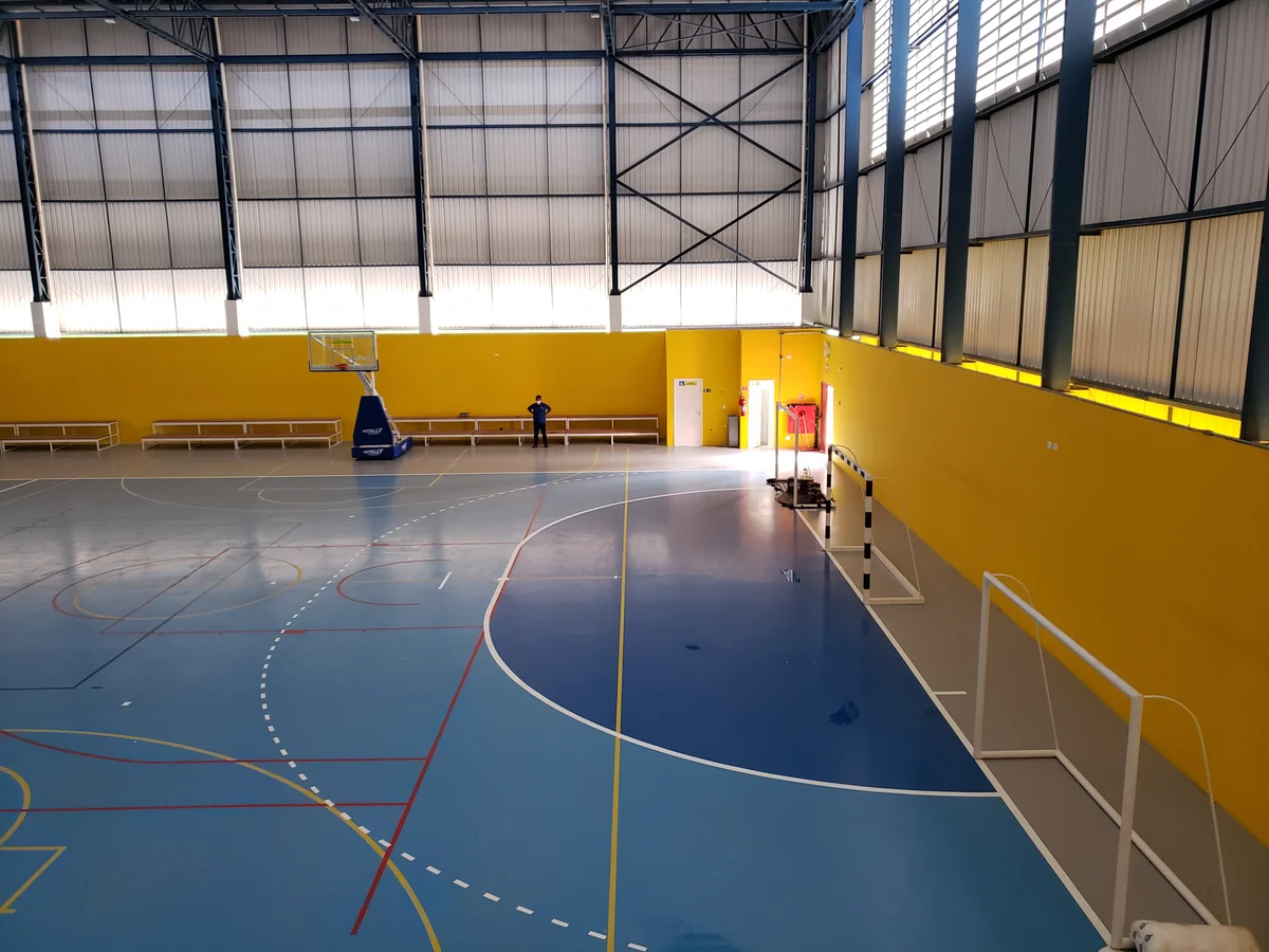 Quadra do ginásio com tabelas de basquete e traves