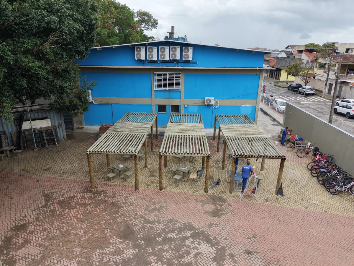 Pátio com pergolados e piso intertravado em frente ao bloco escolar
